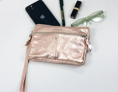 Rose gold crossbody bag with phone, pen, and glasses on a light background