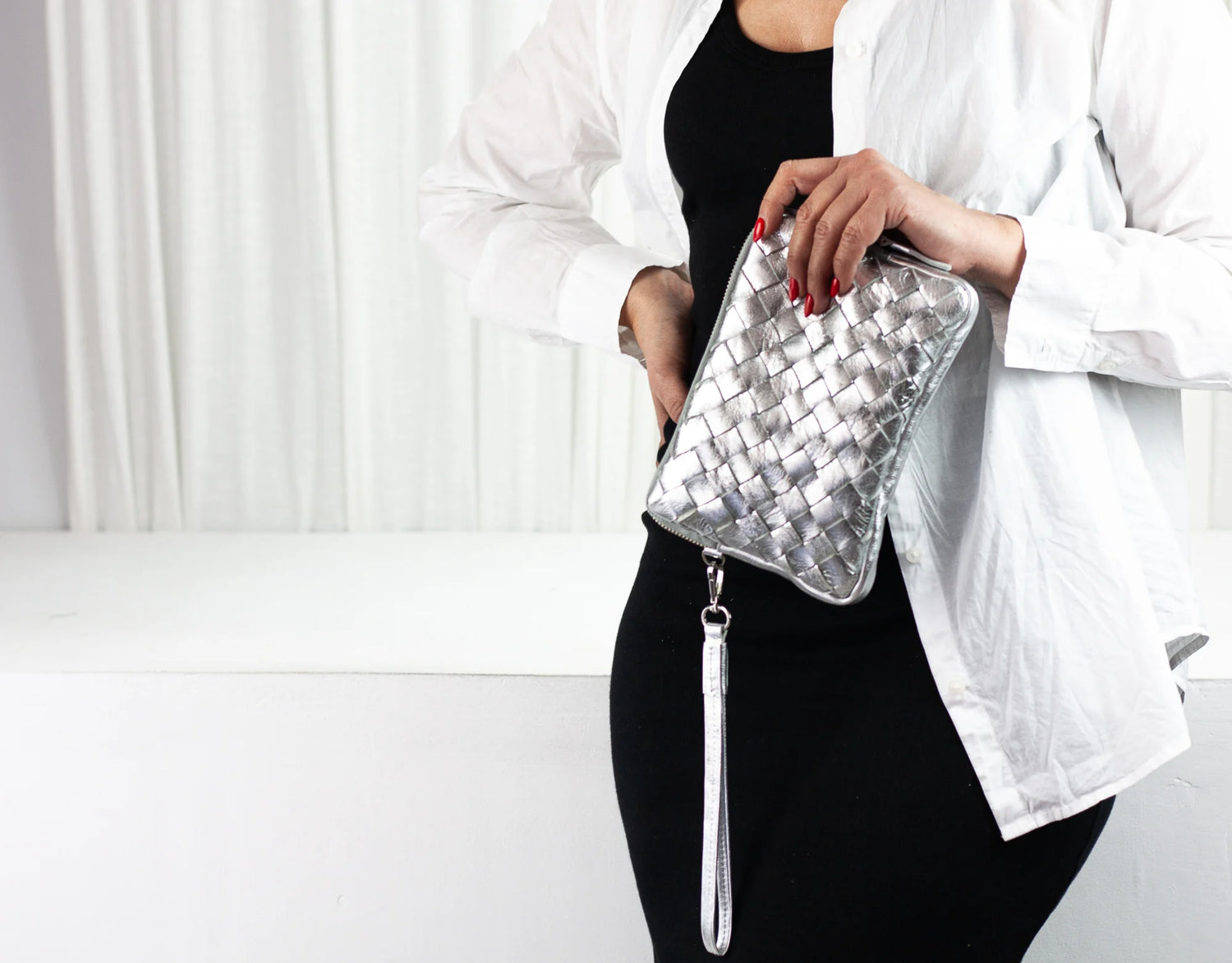 Person holding a silver woven clutch bag against a white background