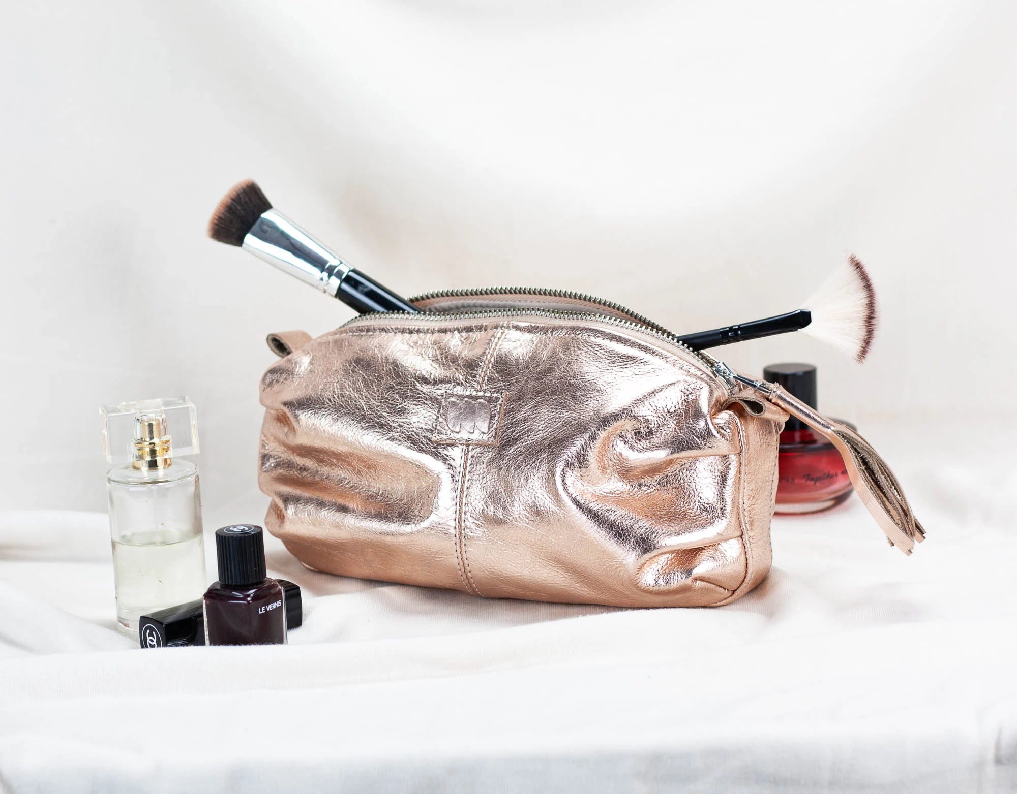 Rose gold makeup bag with cosmetic items on a white background