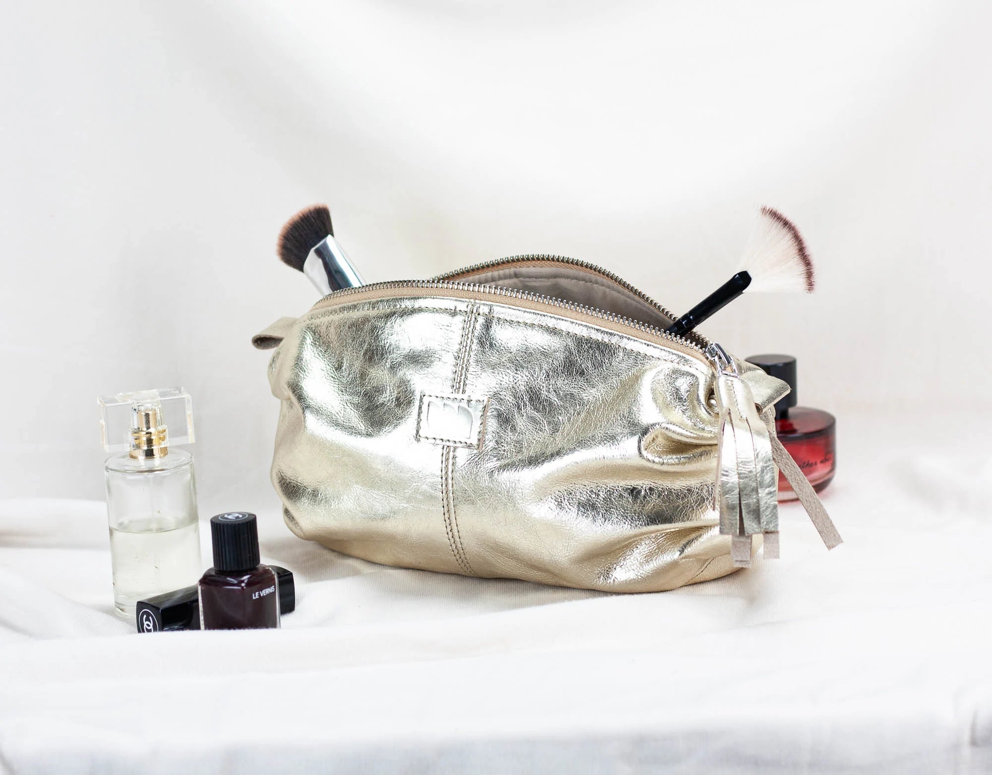 Silver makeup bag with cosmetic items on a white background
