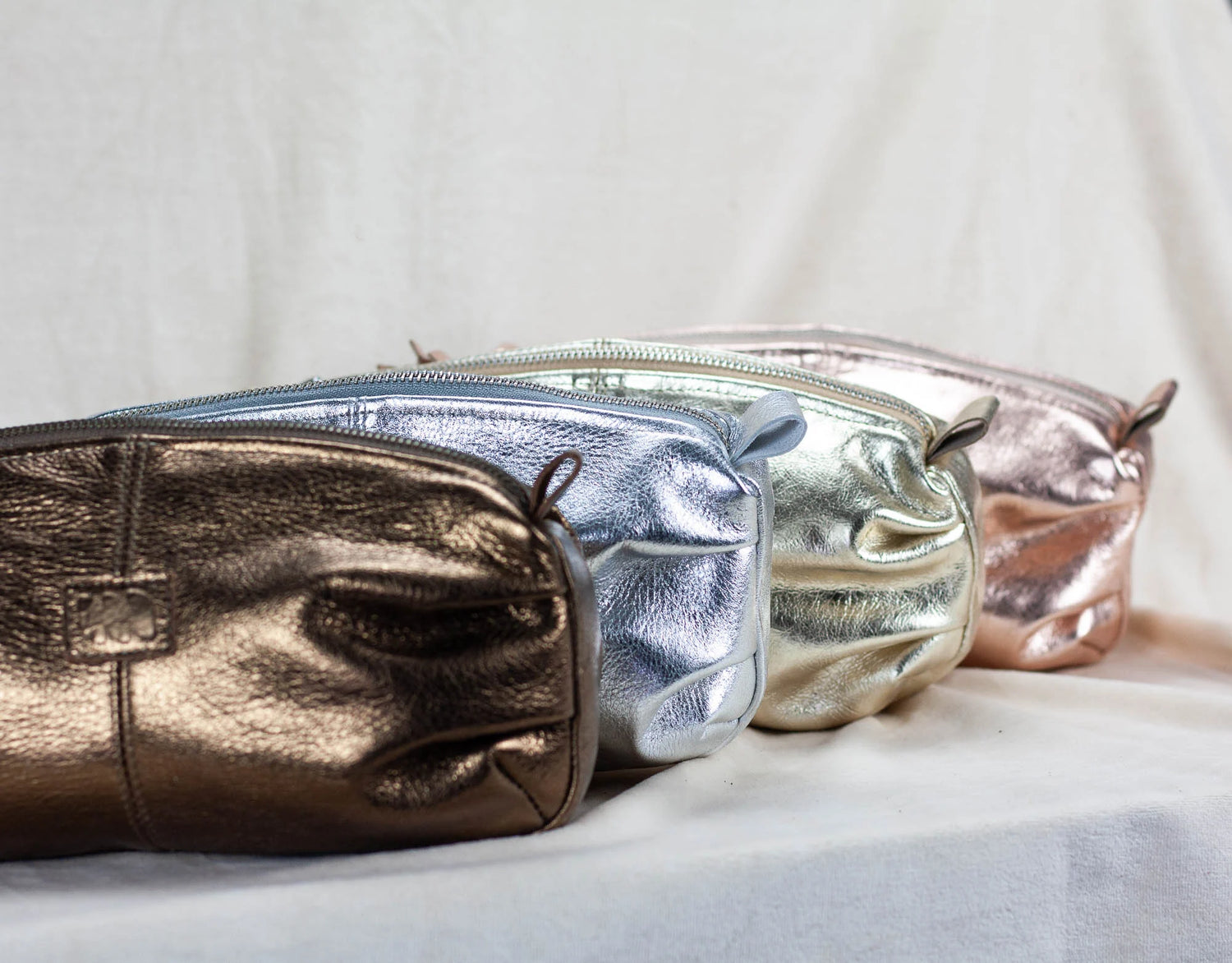 Three metallic pouches in gold, silver, and rose gold on a light background