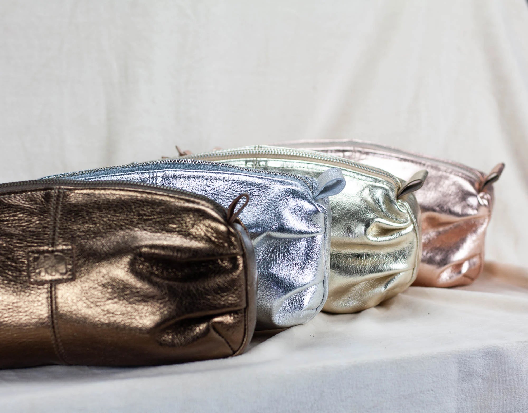 Three metallic pouches in gold, silver, and rose gold on a light background