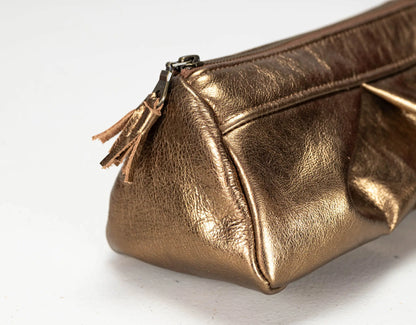 A close-up of a metallic bronze leather cosmetic pouch with a matching leather tassel zipper pull, set against a plain white background.