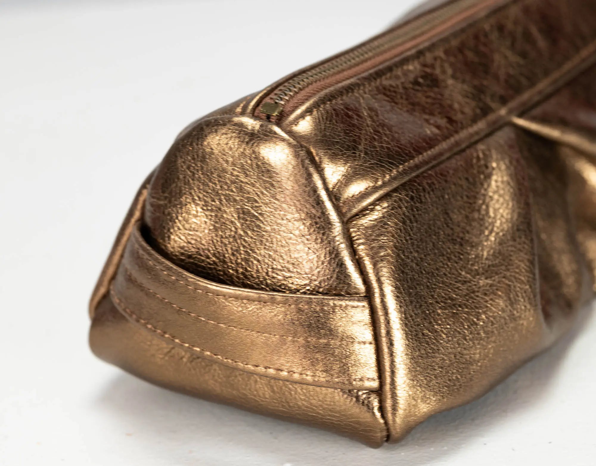 Close-up of a metallic bronze leather zippered pouch on a white background.