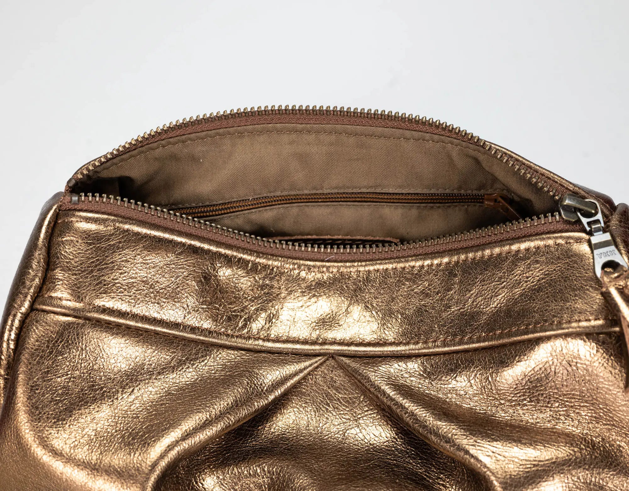 Close-up of a metallic gold leather handbag showing the interior zippered compartment with a silver zipper pull against a plain light background.
