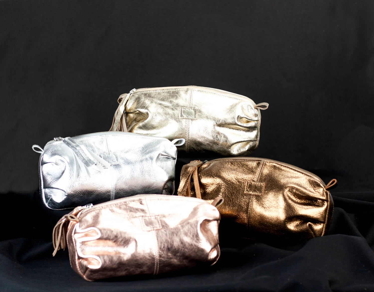 Four metallic pouches in silver, gold, and bronze on a black background