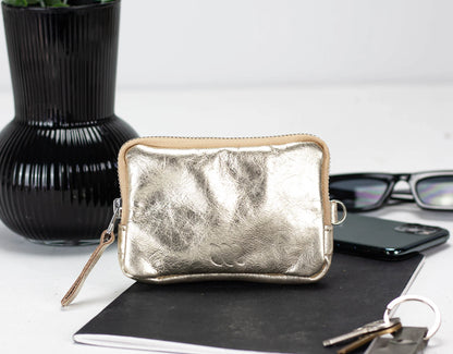 Silver clutch purse on a table with a black vase and glasses in the background