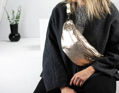 Person wearing a metallic silver fanny pack in a minimal indoor setting.