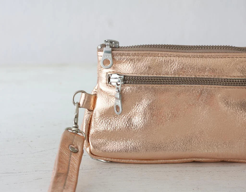 Rose gold clutch bag with a strap on a light wooden surface