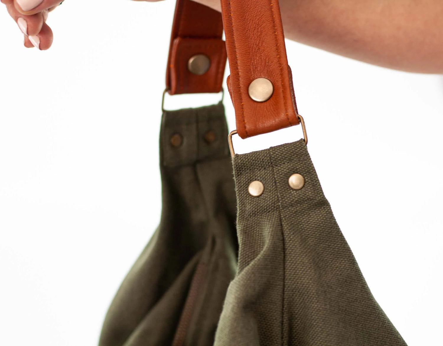 Green bag with brown leather straps held by a person against a white background