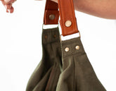 Green bag with brown leather straps held by a person against a white background