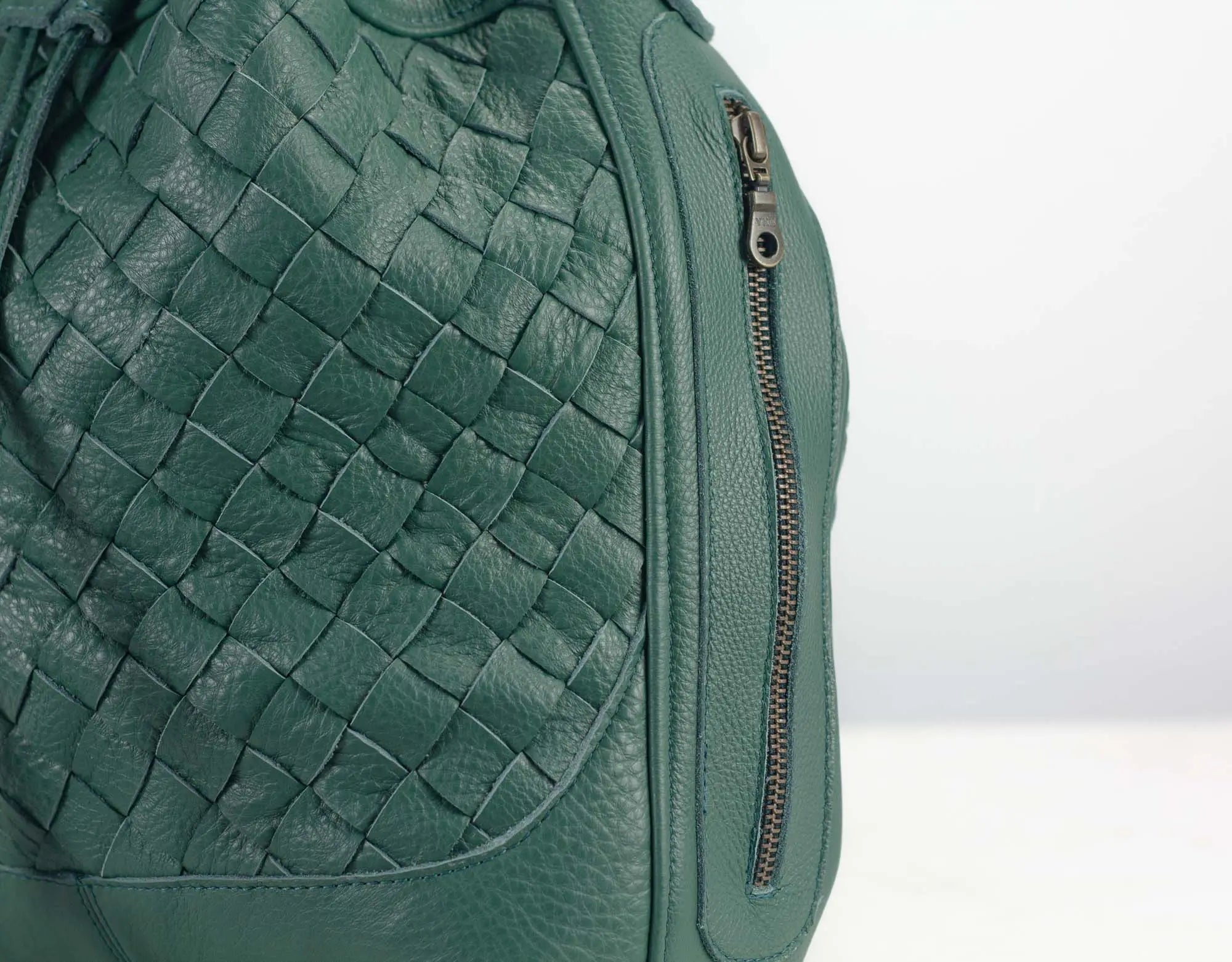 Green woven leather bag with a zipper on a light gray background