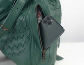 Green textured handbag with a phone in the open zipper pocket on a white background
