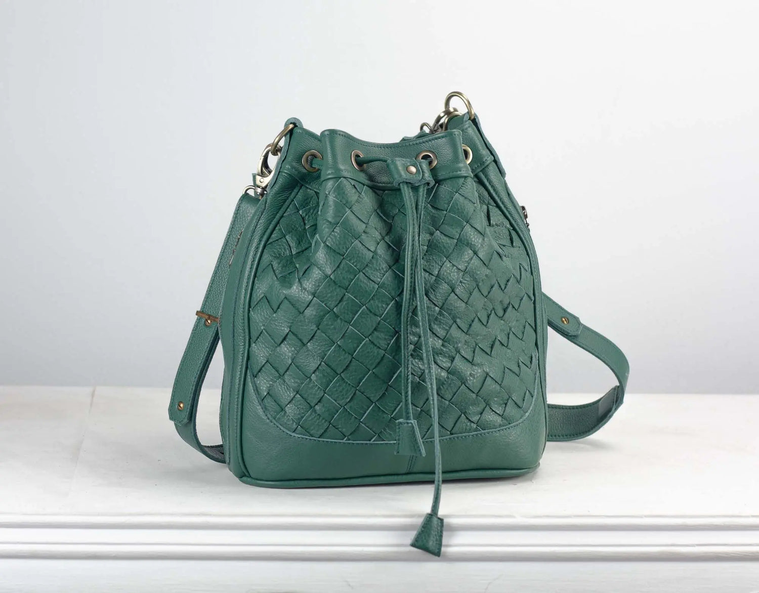 Green woven handbag on a white surface with a light gray background