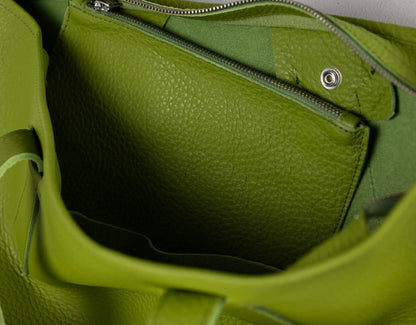 Close-up of the interior of a bright green pebbled leather bag, showing a zippered pocket and metal zipper hardware.