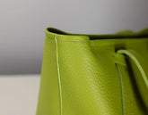 Close-up of a bright lime green pebbled leather bag corner with matching drawstring and visible stitching against a neutral gray background.