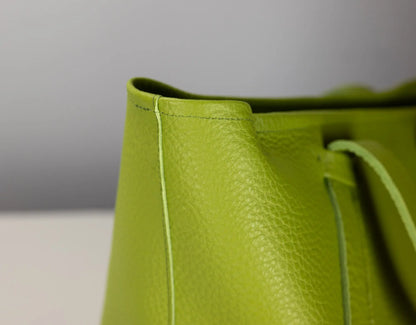 Close-up of a bright lime green pebbled leather bag corner with matching drawstring and visible stitching against a neutral gray background.