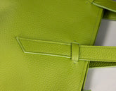 Close-up of a bright lime green pebbled leather bag with a matching strap and tab closure, showing the texture and stitching details.