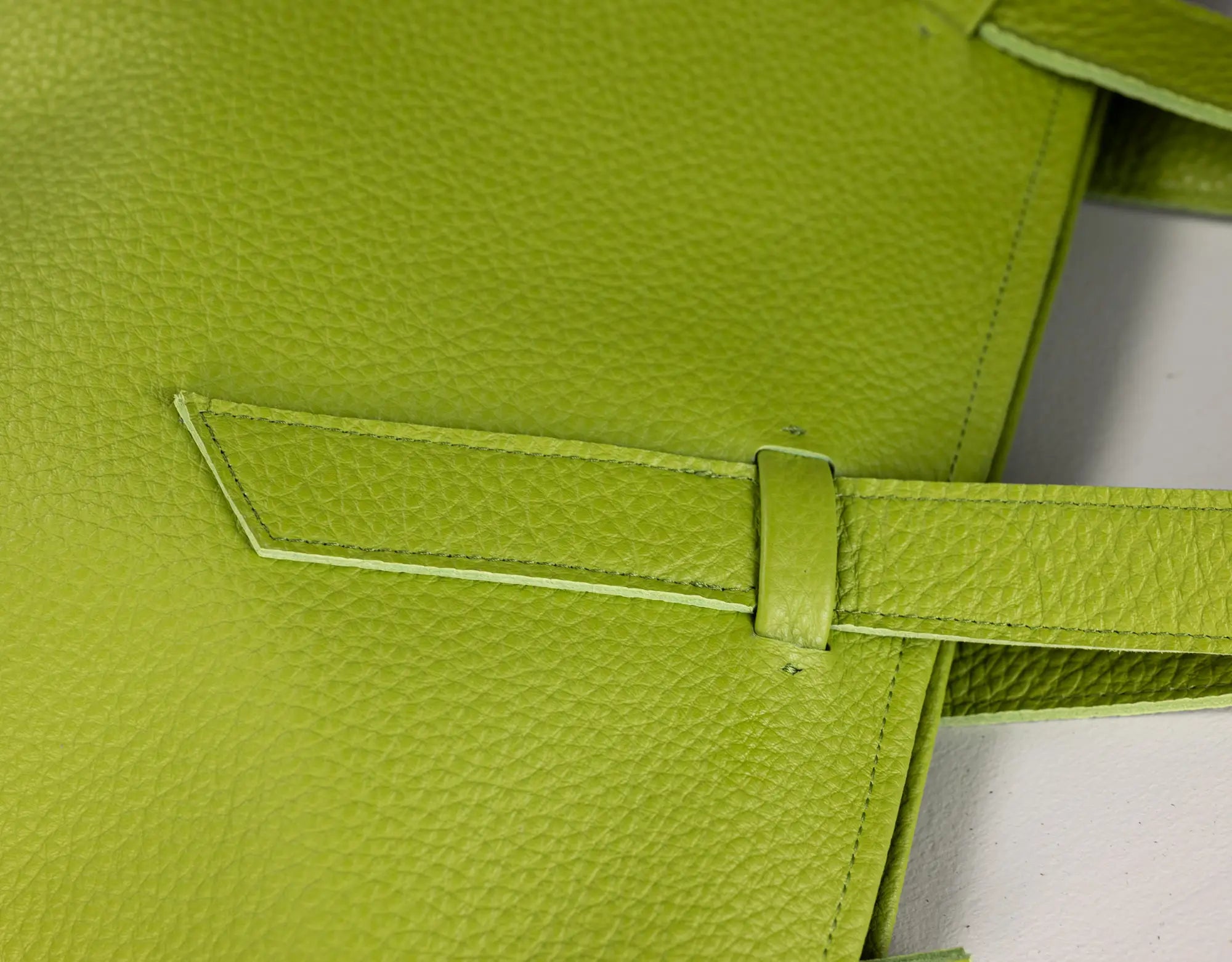 Close-up of a bright lime green pebbled leather bag with a matching strap and tab closure, showing the texture and stitching details.