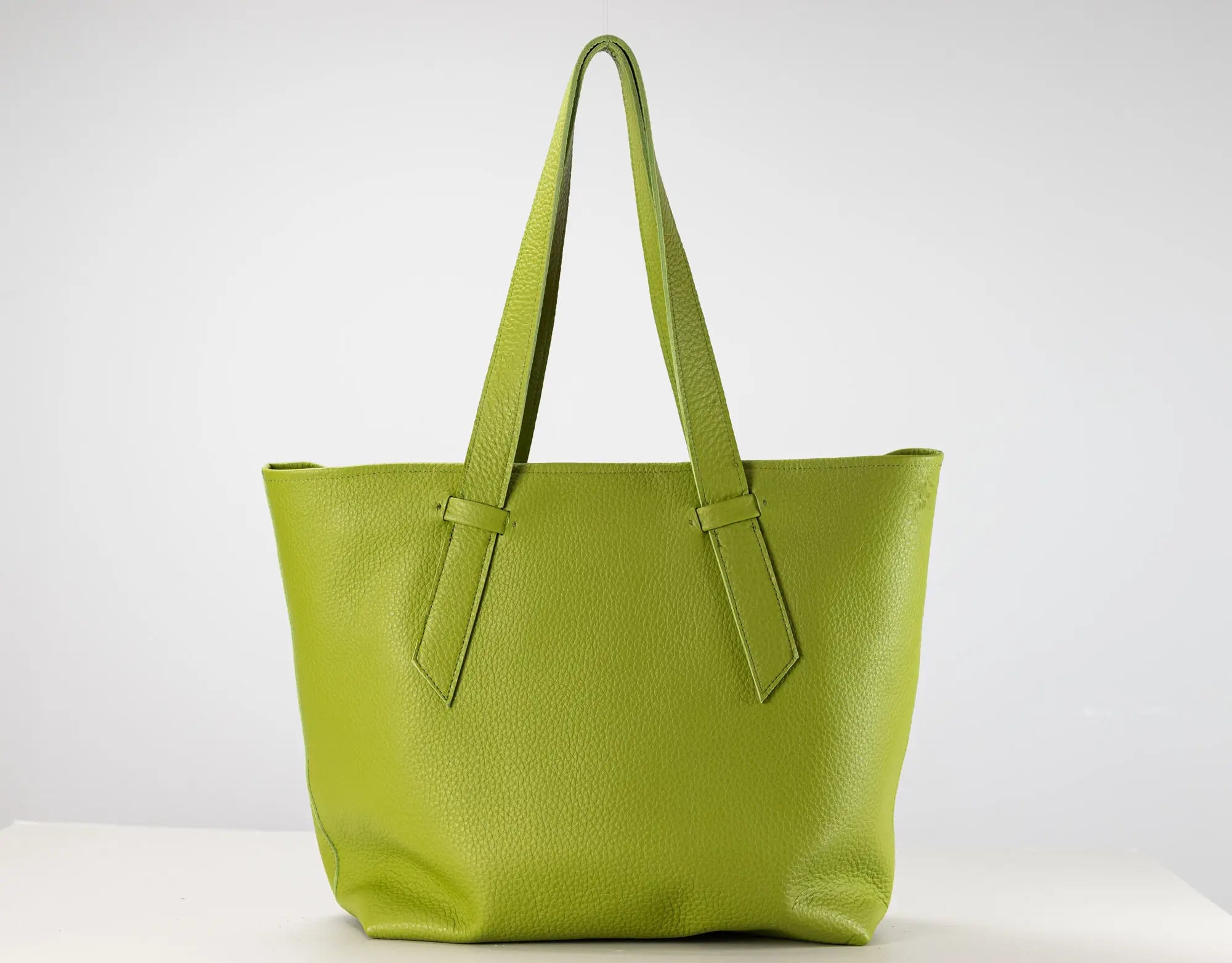 A bright lime green pebbled leather tote bag with two shoulder straps, displayed on a white surface against a light gray background.