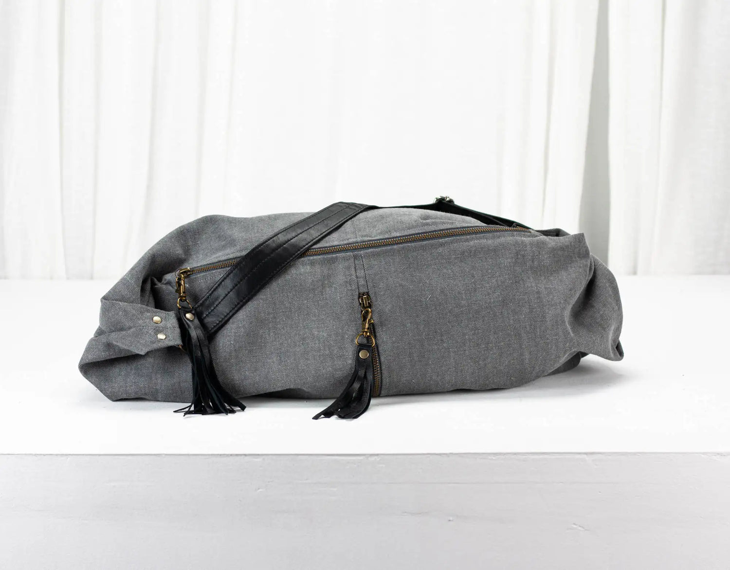Gray duffel bag with black straps on a white background
