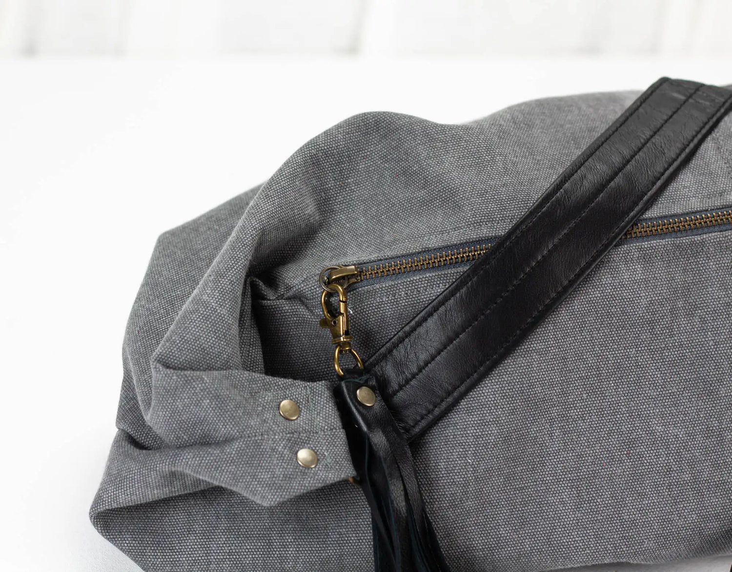 Gray bag with black strap and gold zipper on a white background