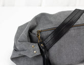 Gray bag with black strap and gold zipper on a white background