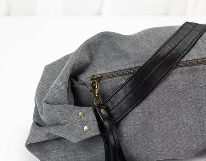 Gray bag with black strap and gold zipper on a white background