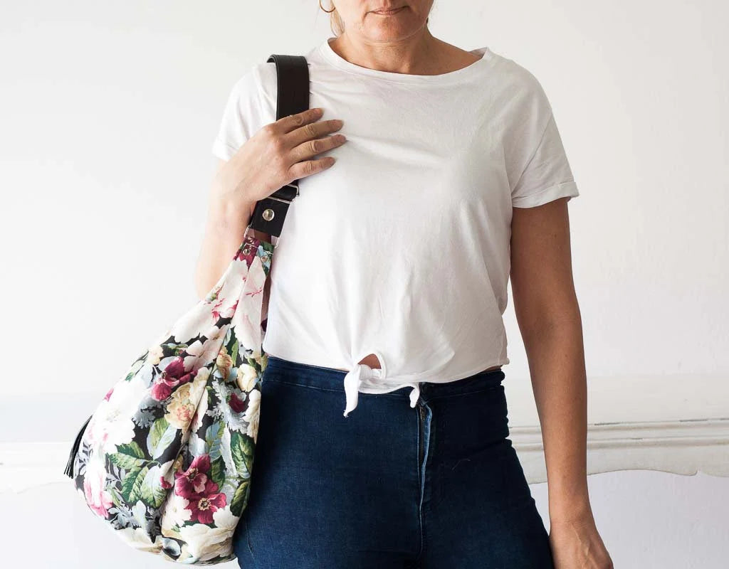 Person wearing a white t-shirt and blue jeans, holding a floral bag against a plain background
