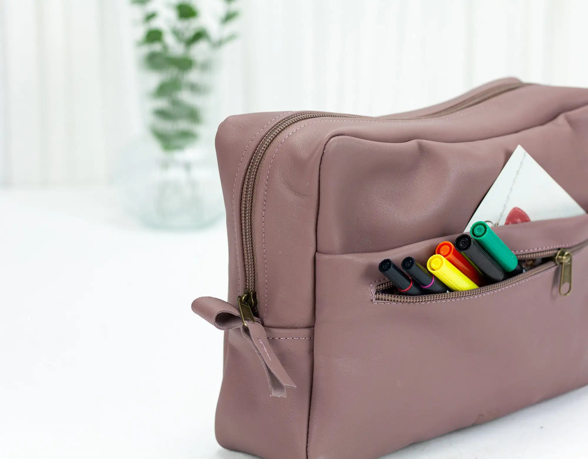 Pink pouch with colorful markers on a white surface