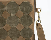 Close-up of a brown leather handbag with geometric pattern and gold zipper pull.