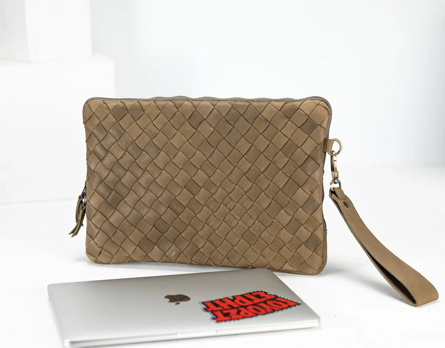 Beige woven clutch bag with a laptop and red book on a white background