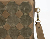Close-up of a brown leather handbag with geometric pattern and gold zipper pull.