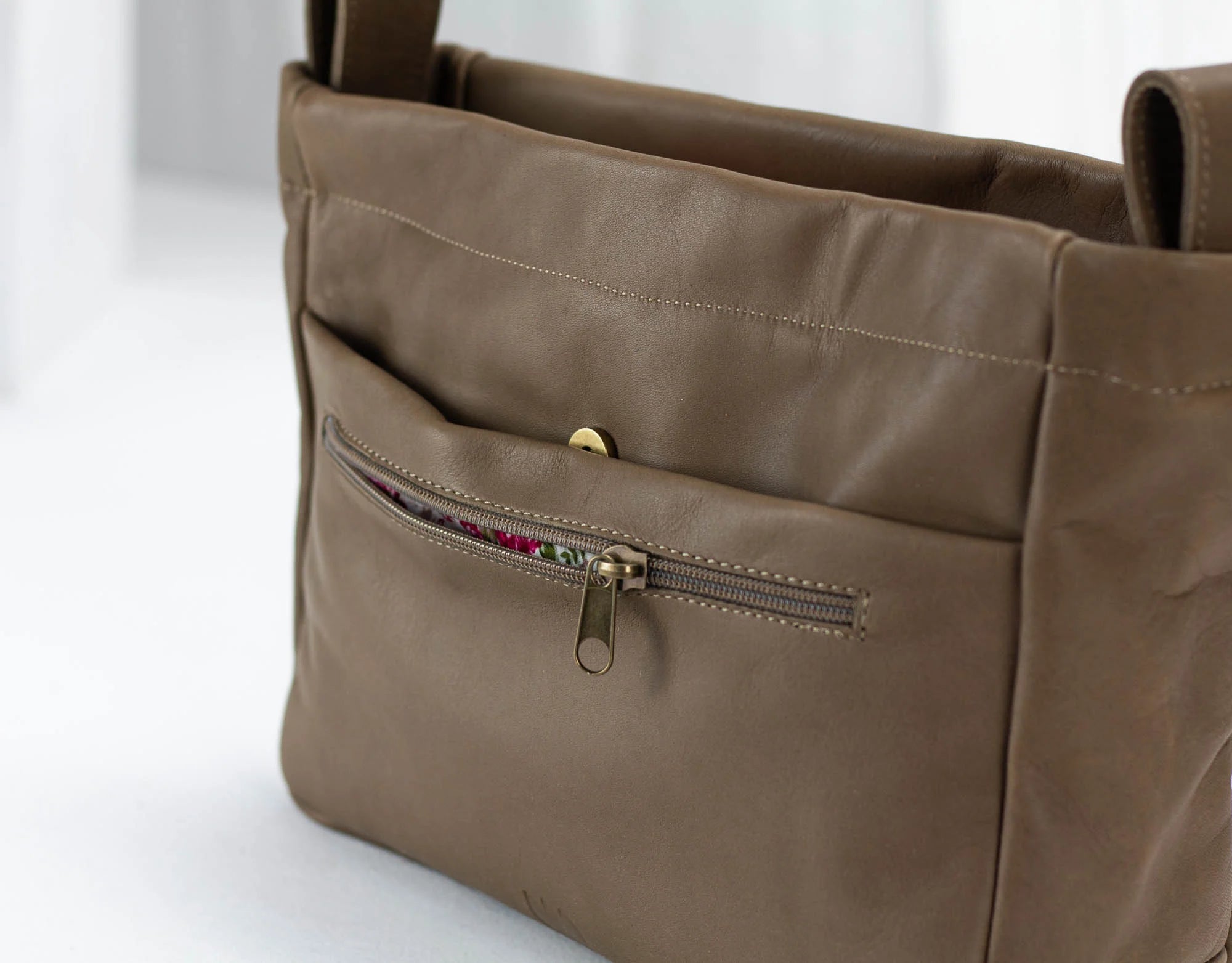 khaki Brown leather handbag with a gold zipper on a white background