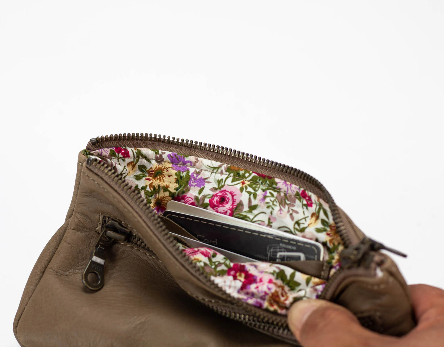 Brown leather clutch with floral interior pocket held by a hand on a white background