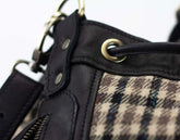 Close-up of a black leather and plaid fabric bag with metal hardware.