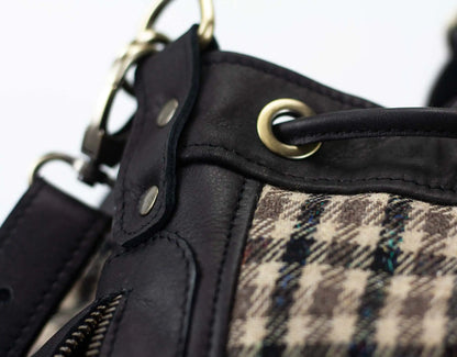 Close-up of a black leather and plaid fabric bag with metal hardware.
