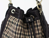 Close-up of a plaid handbag with black straps and gold hardware.