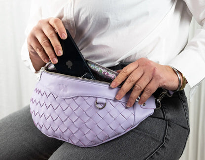 Person holding a purple woven fanny pack with a phone in it.
