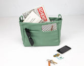 Green bag with compartments holding books, a phone, and keys on a white background