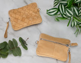 Two woven beige handbags on a marble surface with green leaves.