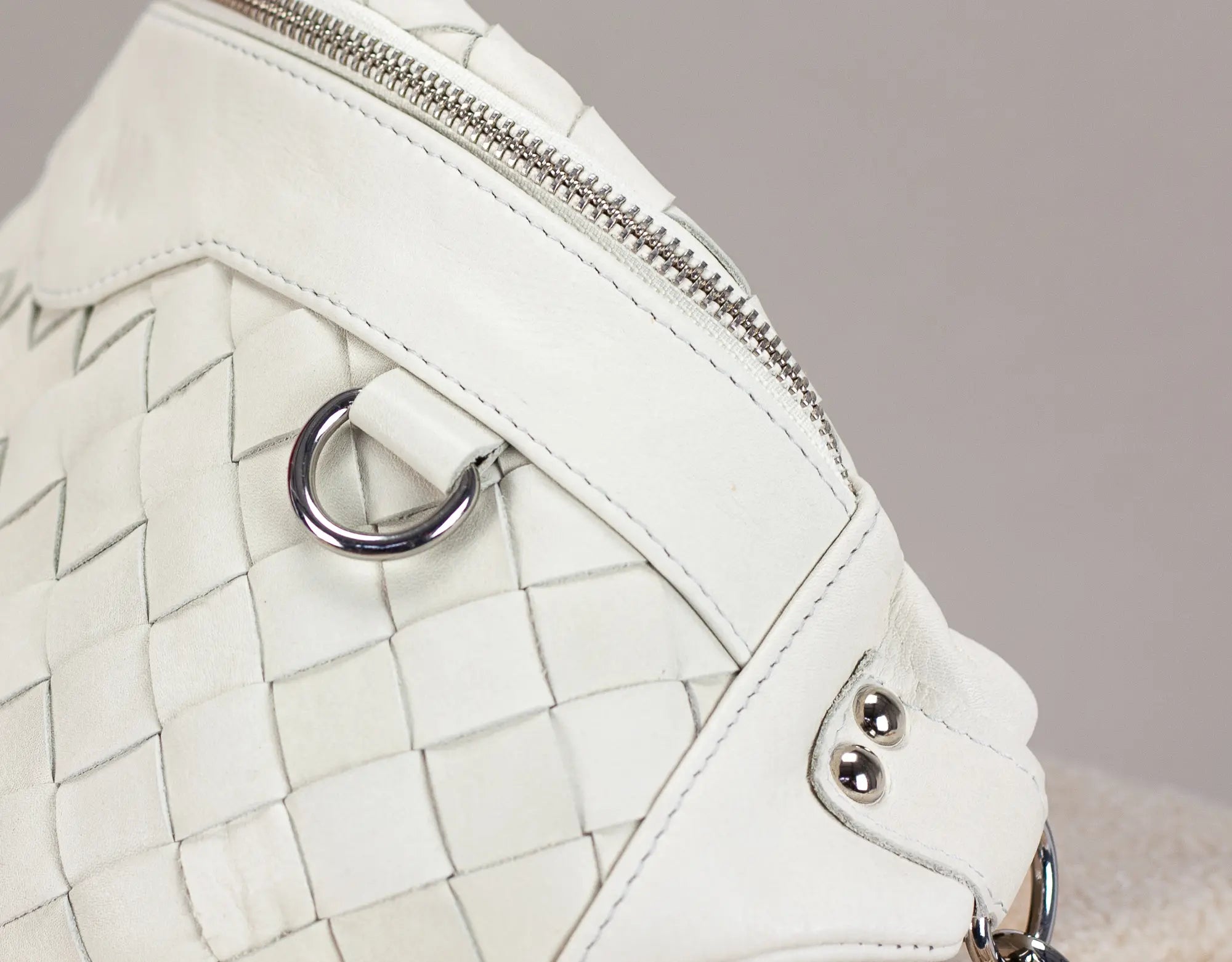Close-up of a white quilted handbag with a metallic clasp on a neutral background