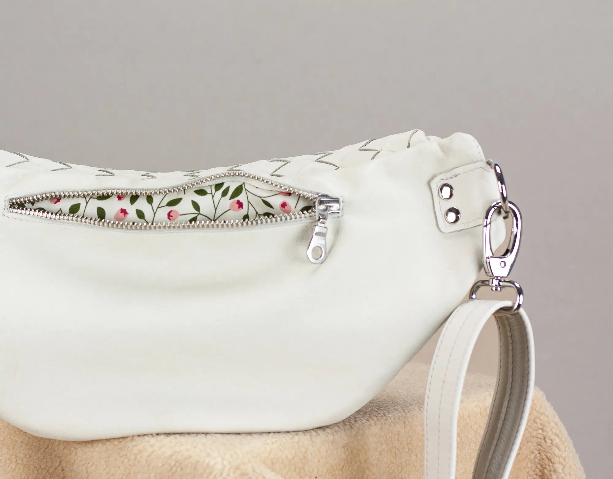 White handbag with floral zipper pull on a gray background