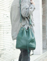 Person holding a green leather bucket bag against a light background