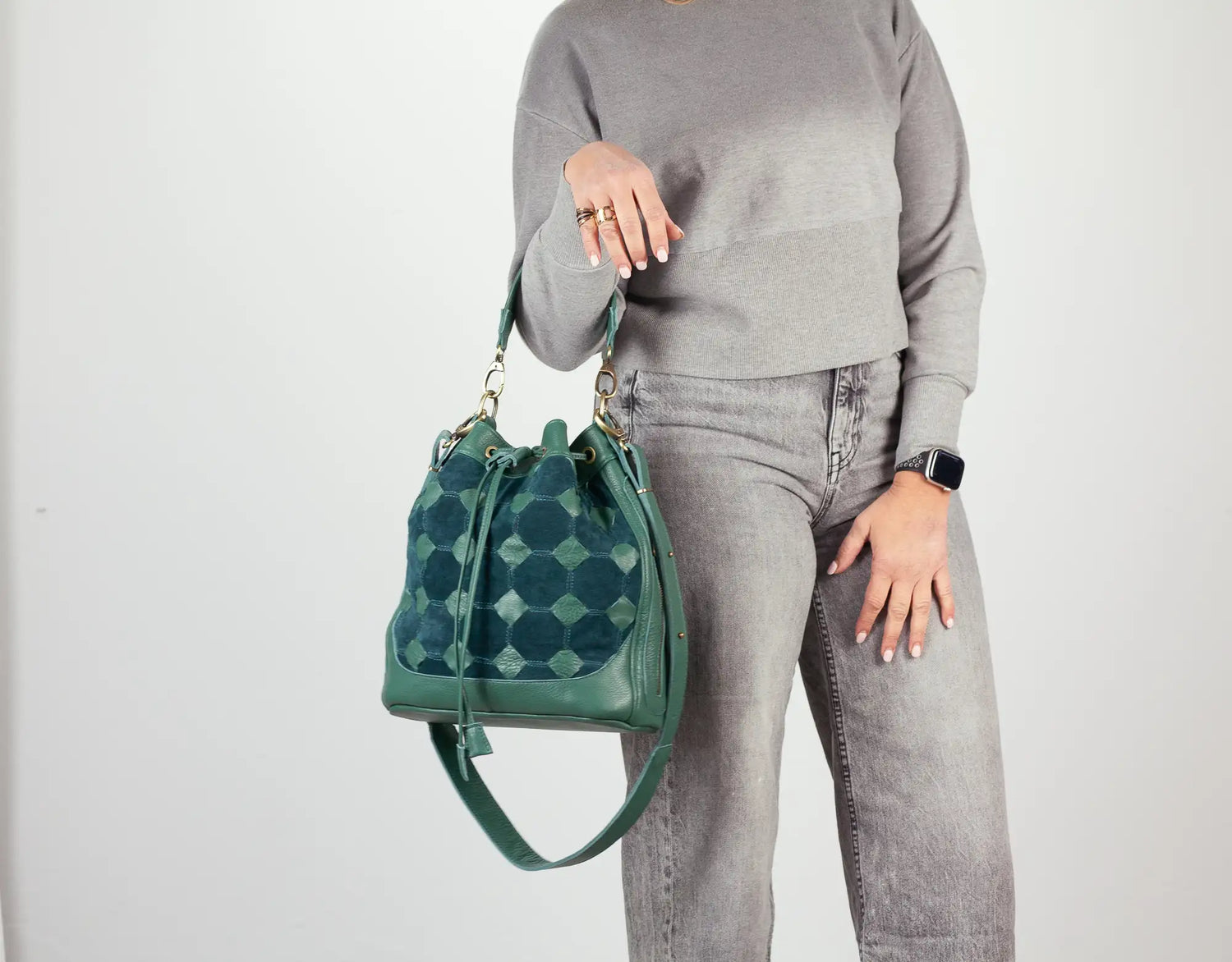 Person holding a green handbag with a geometric pattern on a plain background