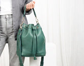 Green leather bucket bag held by a person against a white background