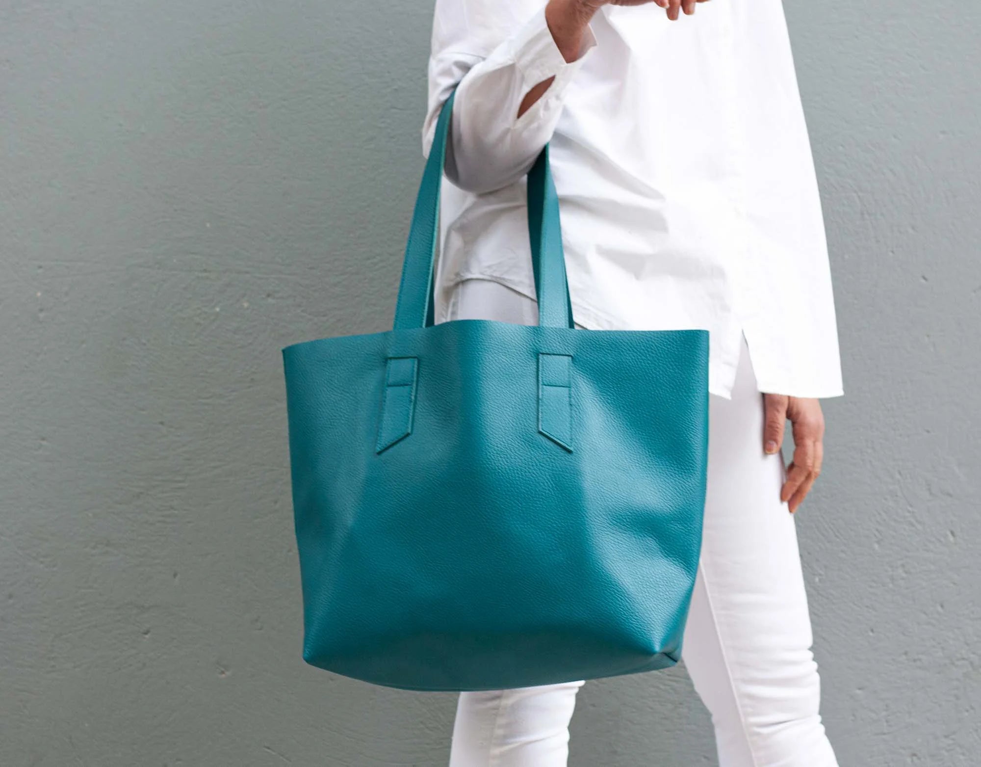 Person holding a teal tote bag against a gray background
