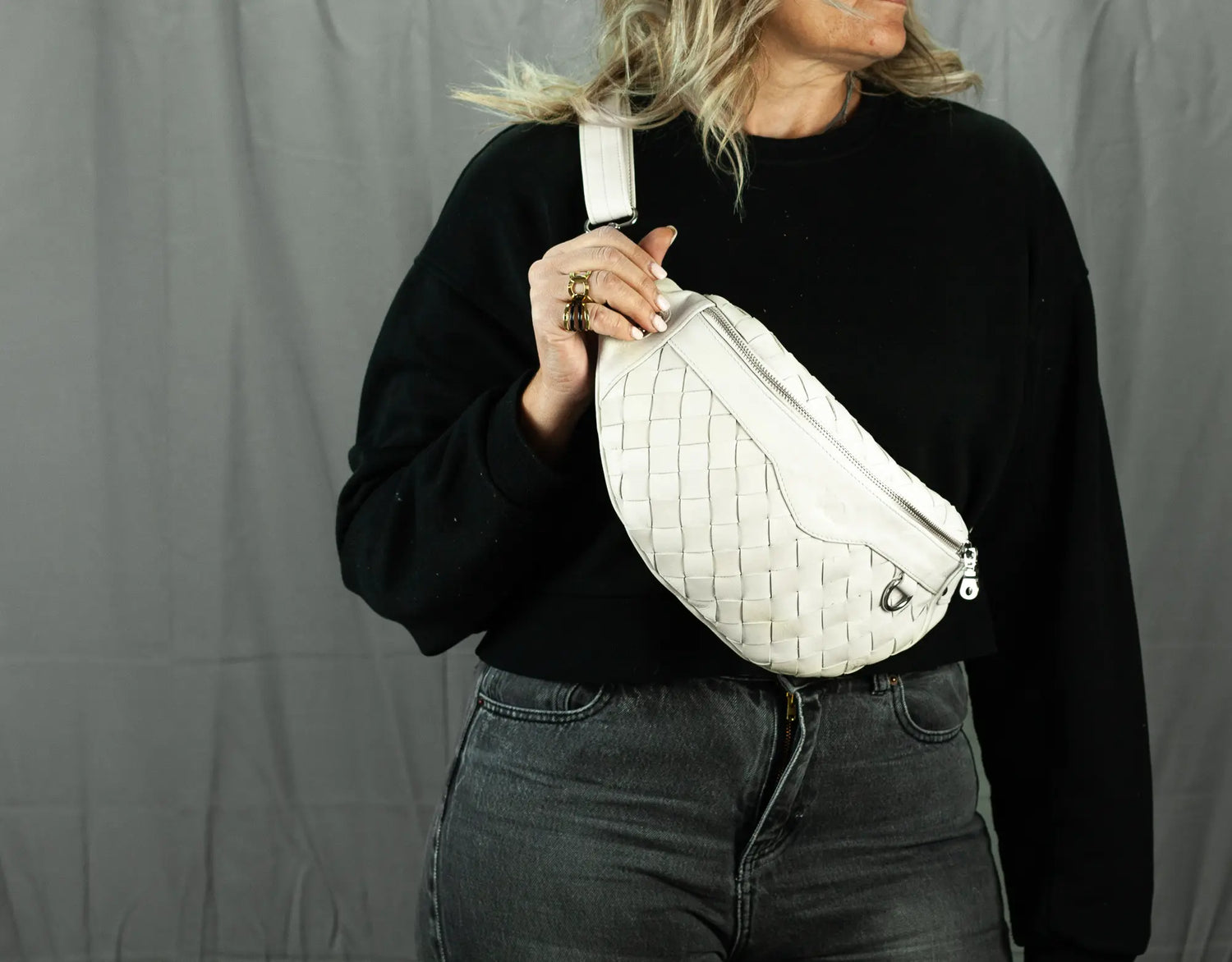 Person holding a white woven bag against a gray background