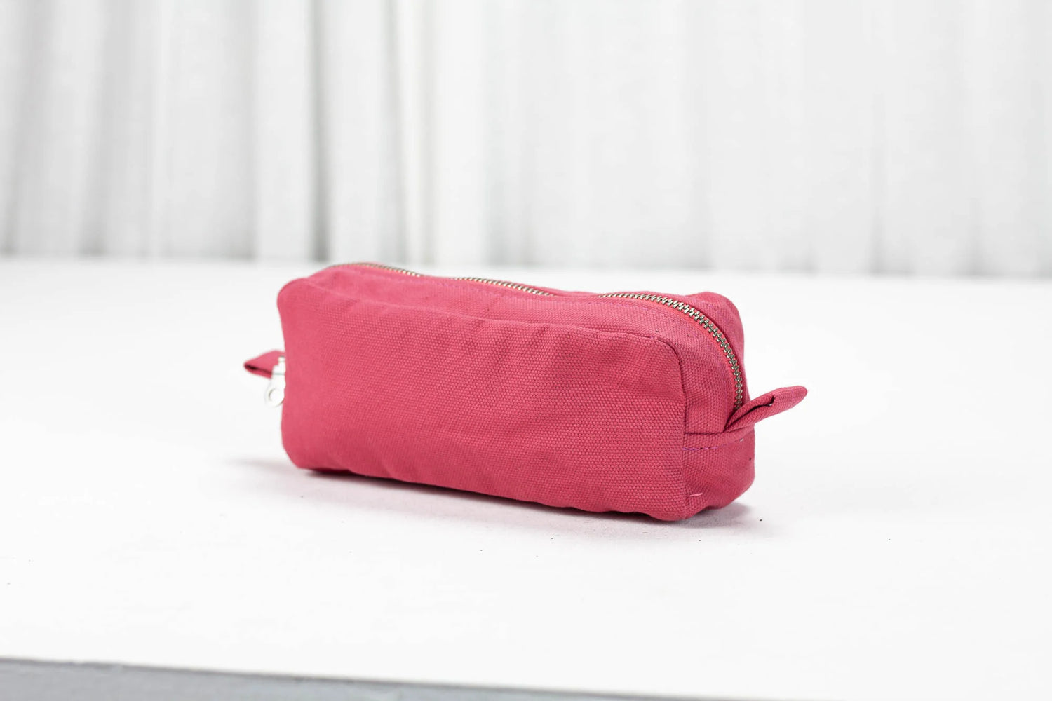 Pink cotton toiletry bag on a white surface with a light gray background