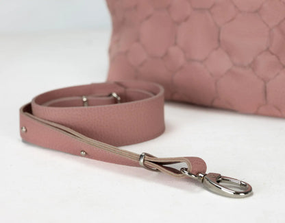 Pink leather dog leash with metal clip on a white surface, with a pink textured bag in the background.